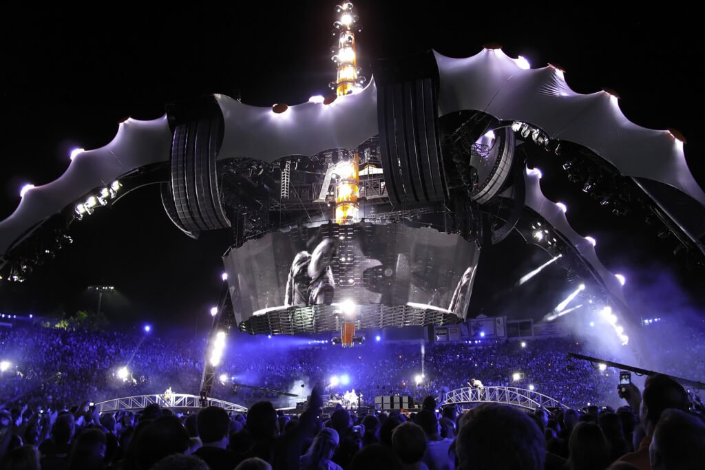 A dynamic concert at night with a massive stage illuminated by vivid blue and yellow lights, captivating a large crowd.