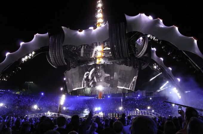 A dynamic concert at night with a massive stage illuminated by vivid blue and yellow lights, captivating a large crowd.