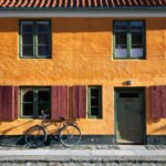 London A classic bicycle leans against a vibrant orange building, adding timeless charm. Green shutters frame the windows.