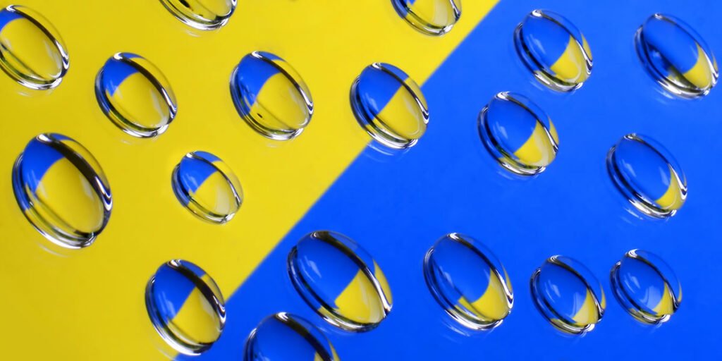 Water droplets resting on a vibrant yellow and blue surface, seamlessly blending colors through their reflections.