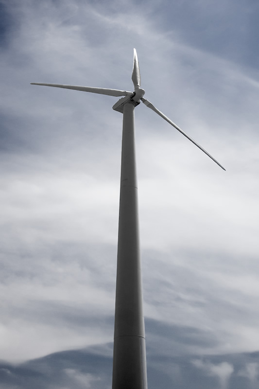 A tall white wind turbine stands prominently against a cloudy sky, its blades poised to catch the wind.