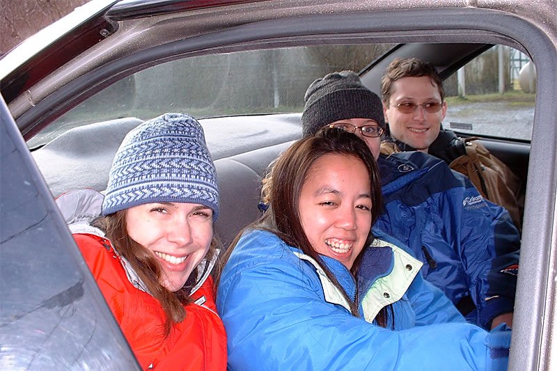 A family of three smiling in a car, bundled up for cold weather.