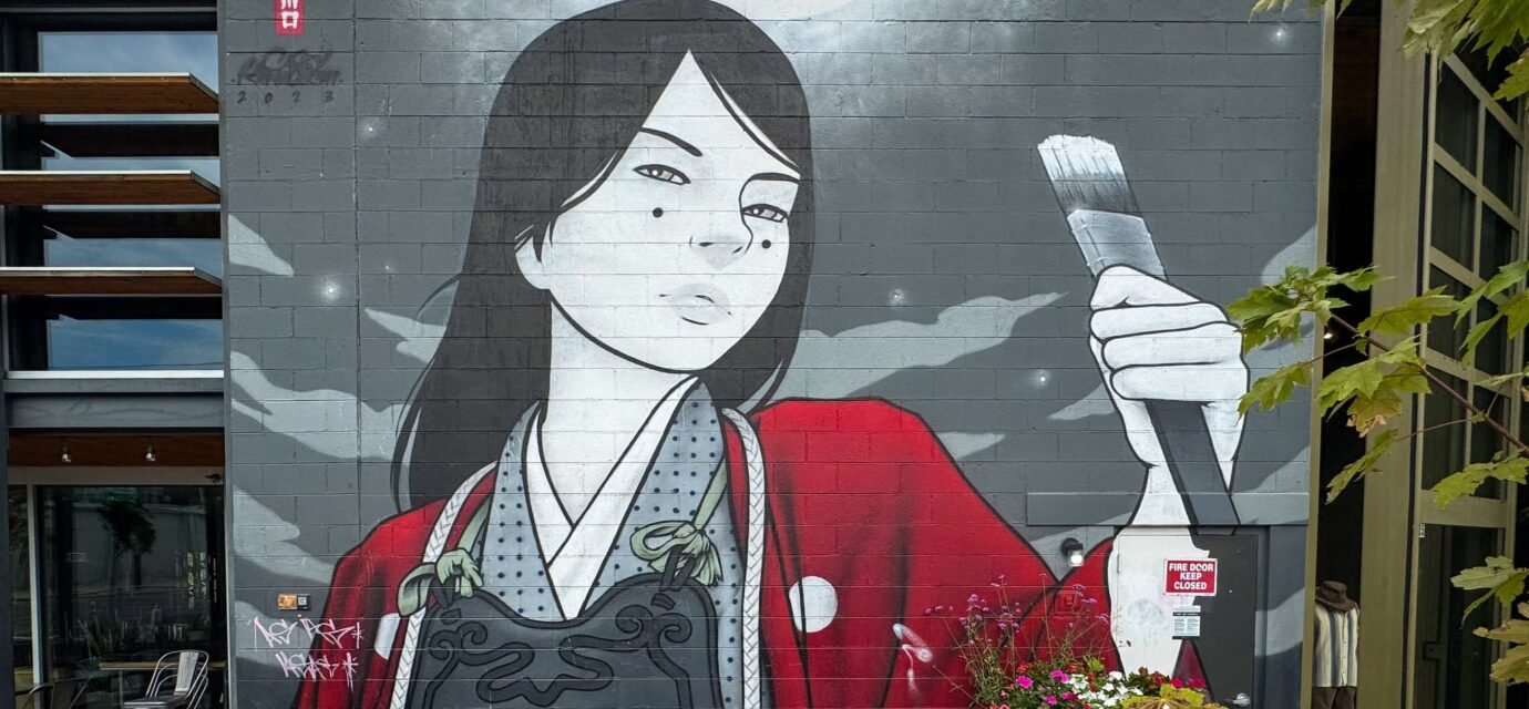 A mural of a woman dressed in traditional attire holds a large paintbrush. The artwork features bold reds and blacks against a grayscale background.