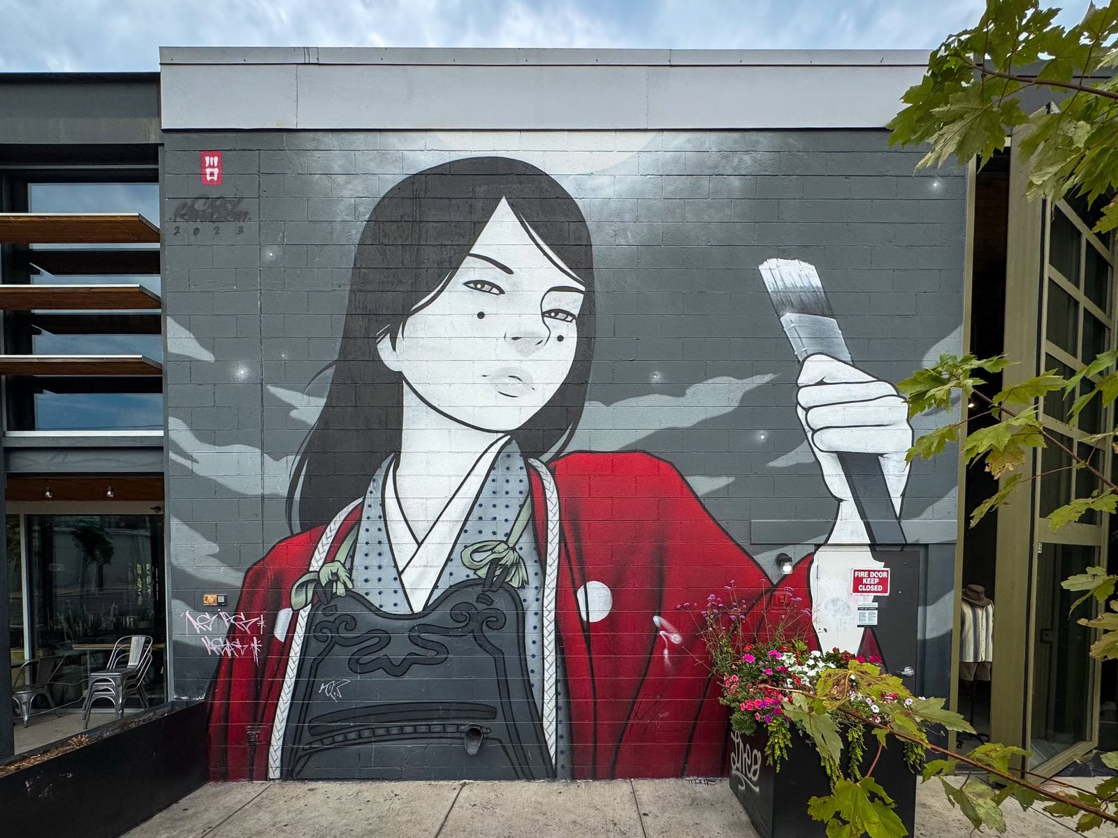 A mural of a woman dressed in traditional attire holds a large paintbrush. The artwork features bold reds and blacks against a grayscale background.