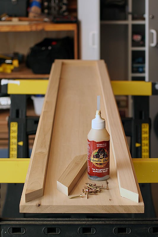 A partially assembled wooden structure with glue and nails on a workbench.