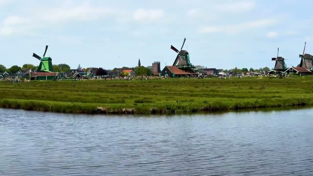 Traditional Dutch windmills and colorful buildings line a green bank beside a calm canal. This scenic view captures the iconic landmarks of the region.