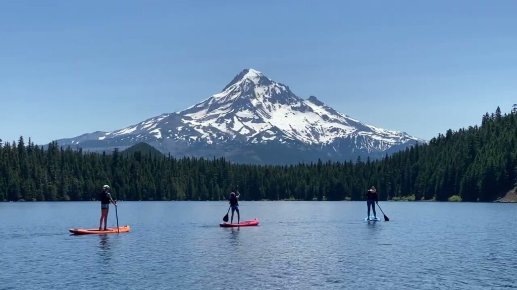 People paddleboarding on a calm lake with Mount Hood in the background. View of the Pacific Northwest landscape with snow-capped peaks.