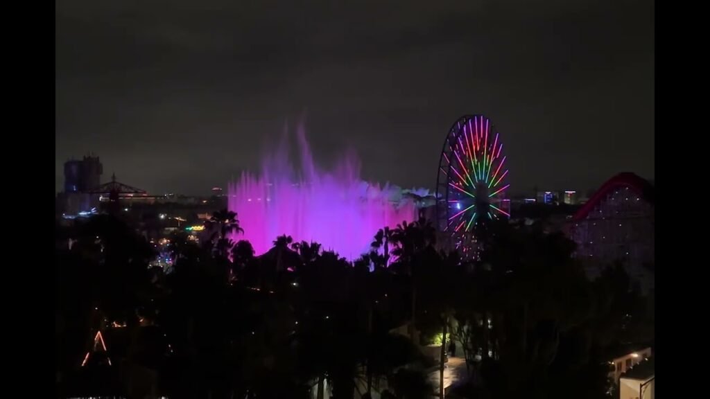 A colorful fountain illuminated in purple and a rainbow Ferris wheel against a night sky.