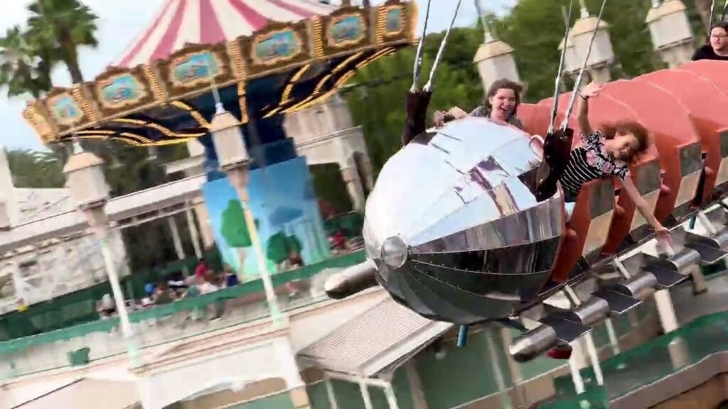 A group of people enjoying a spinning carnival ride with a large striped tent in the background.
