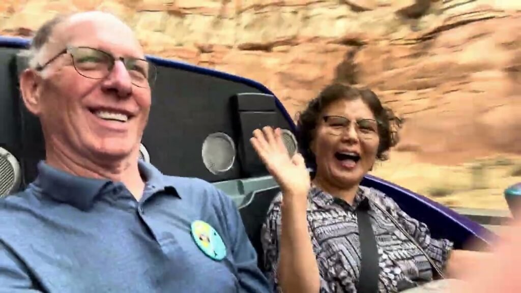 A fun and energetic photo taken during a thrilling ride at a theme park. Two friends share smiles while seated in a vehicle that speeds past red rock formations.
