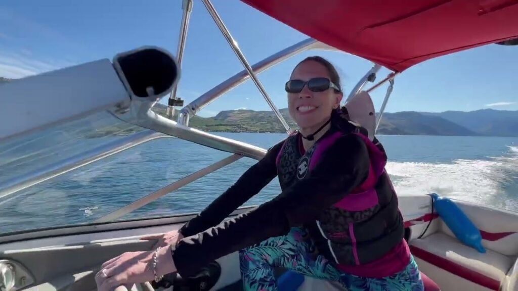 A person enjoys sailing on a boat with a red canopy under a blue sky with mountains in the background.