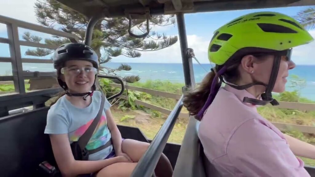 Two riders on an open-air vehicle enjoying a scenic coastal landscape.