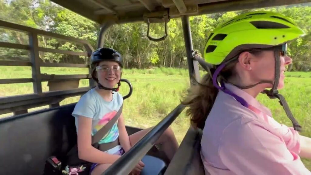 Passengers wearing safety helmets enjoy a guided tour through vibrant green vegetation.