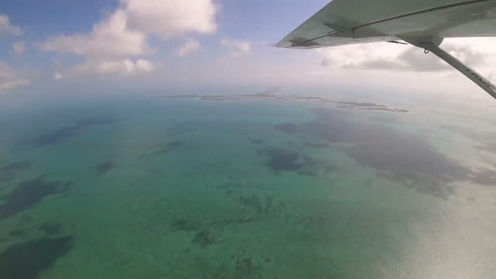 Aerial view of a shallow, turquoise lagoon with sandbars and an airplane wing in the foreground.