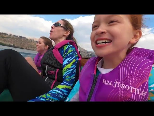 People wearing purple life jackets enjoy a boat ride on a lake with mountains in the background.