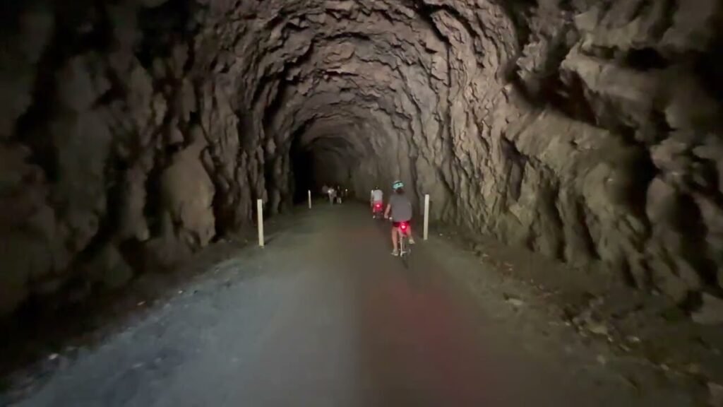 A view from inside a long, rocky mining tunnel with a smooth paved pathway leading toward the exit.