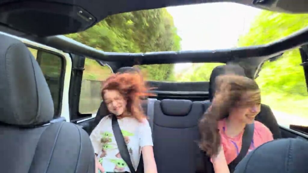 Two children with hair blowing in the wind while riding in a Jeep on a road trip in the Pacific Northwest.