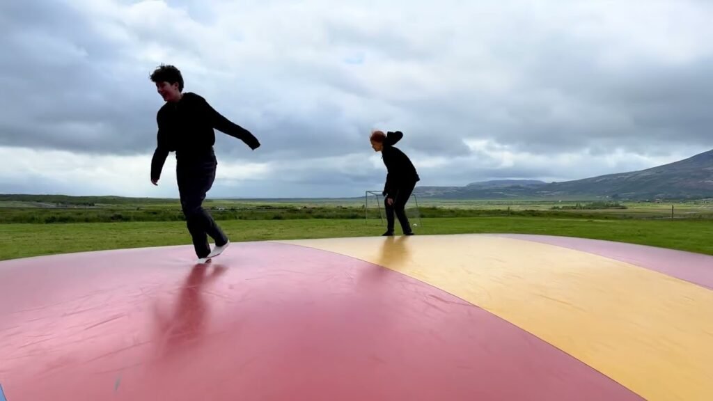 A photo of two people playing on the gigantic pink and yellow ping pong table sculpture at Dungeness, UK.