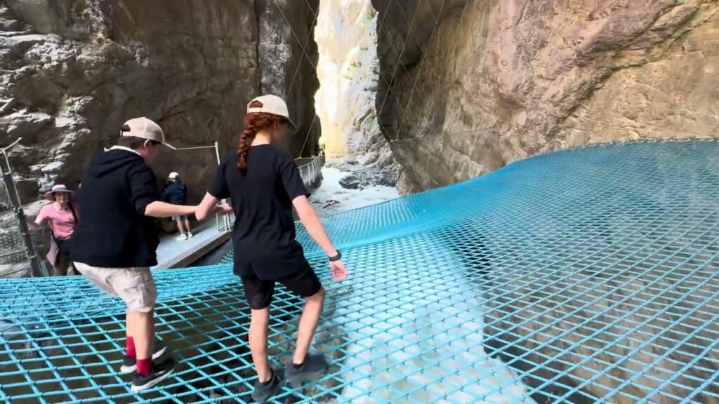 Travelers walk carefully across a blue net bridge in a rocky canyon.