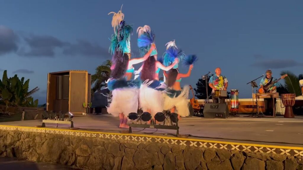 Dancers in grass skirts perform with drums at sunset.