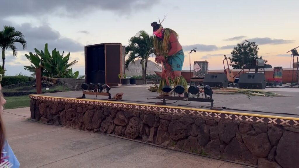 An outdoor stage with a stone wall and palm trees under a cloudy sky.