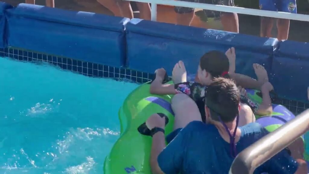 Three individuals relaxing on green inflatable rafts in a pool, wearing blue shirts and sunglasses.