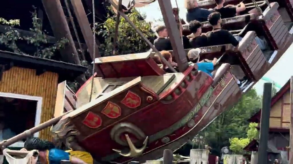 A group of people enjoying a thrilling ride in an amusement park, seated in a large red ship-shaped vehicle.