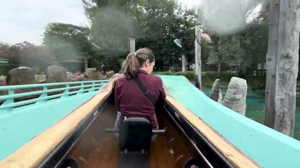 A person rides a log flume through a lush, green area with stone pillars.