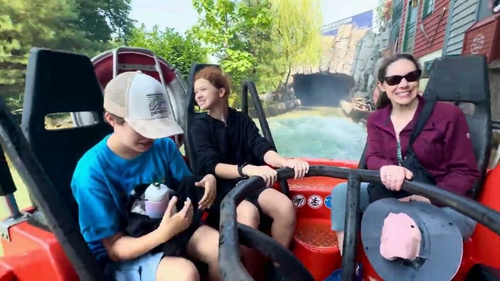 Family enjoying a river ride on a red boat with safety harnesses in a scenic setting.
