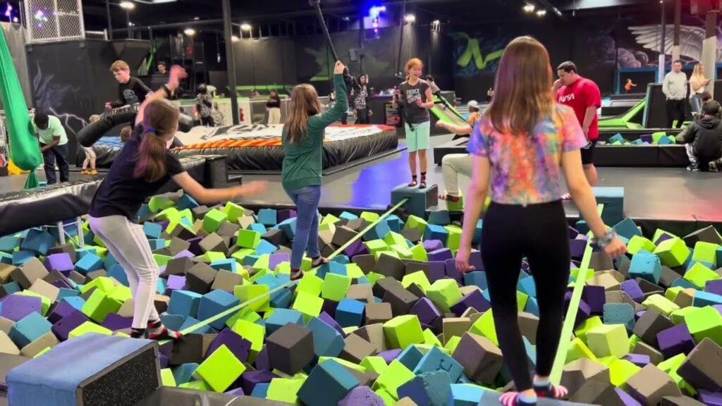 Individuals enjoying a colorful foam pit filled with bright cubes at an indoor trampoline park.