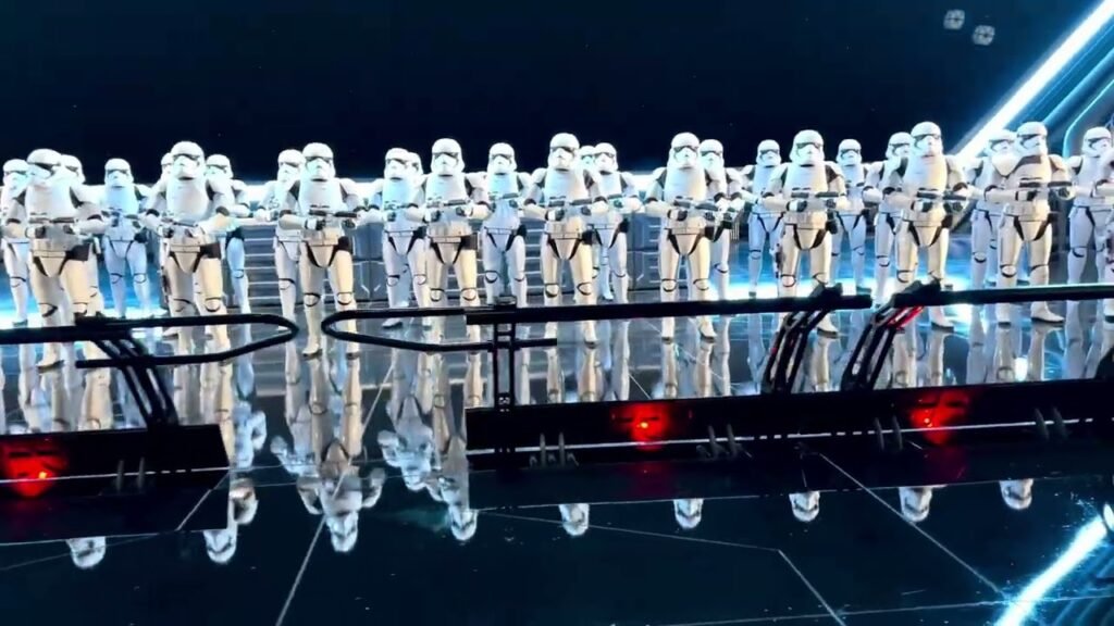 A large group of white-armored characters performing on a stage at night. The background is dark with blue lights and a reflective floor.