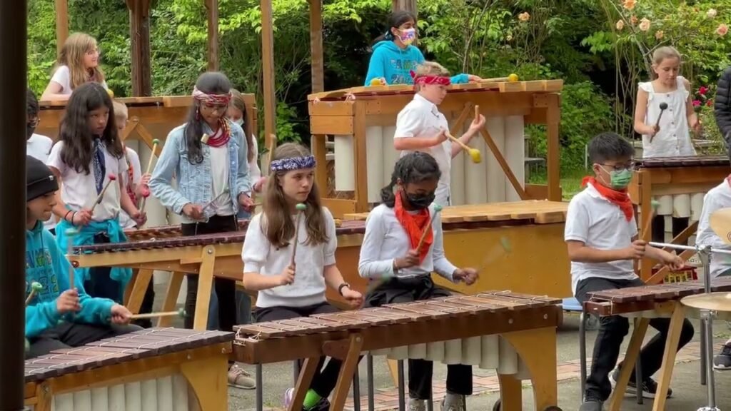 A group of young people playing wooden percussion instruments outdoors, engaged in a musical activity at a camp.