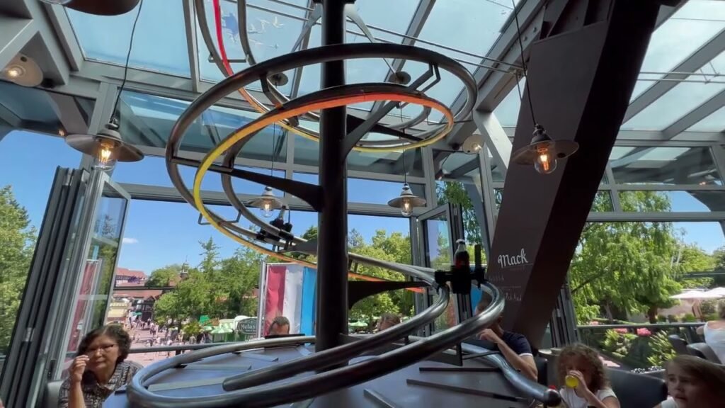 A view of the rotating rings inside the Space Needle observation deck with people and an outdoor garden visible through the glass walls.