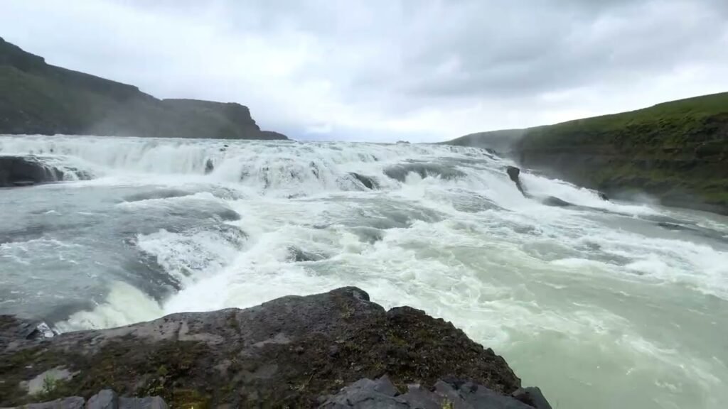 A wide river with turquoise waters flows powerfully through green landscape.