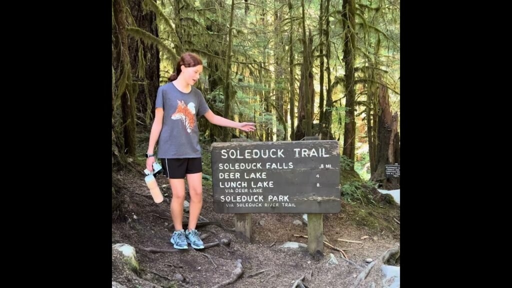 Hikers explore the Soleduck Trail sign in a lush Pacific Northwest forest.