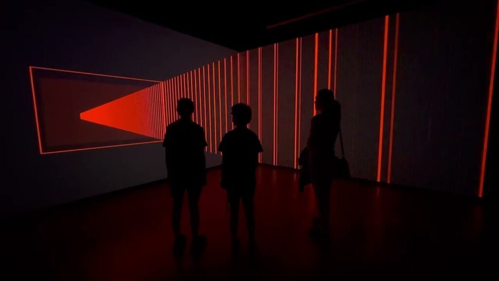 Silhouettes of three people standing in a dark gallery illuminated by red light installations.