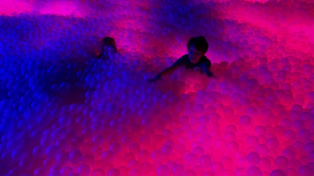 Playful moments in a water feature illuminated by vibrant neon pink and blue lights.