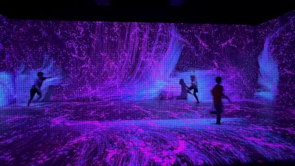 Visitors explore an interactive room with vibrant purple and blue projection mapping.