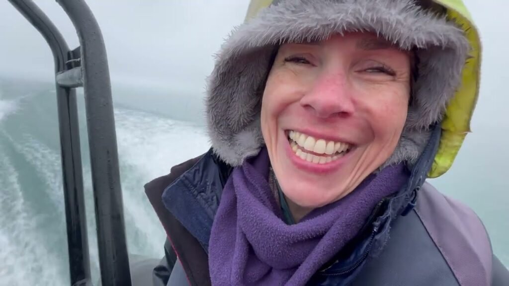 Smiling traveler wearing a purple scarf and yellow hooded jacket. Enjoying a boat ride through cold, misty waters.