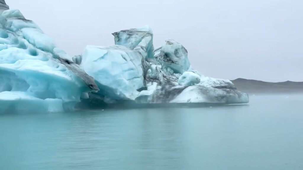 A large, textured iceberg floats in calm, teal glacial water.