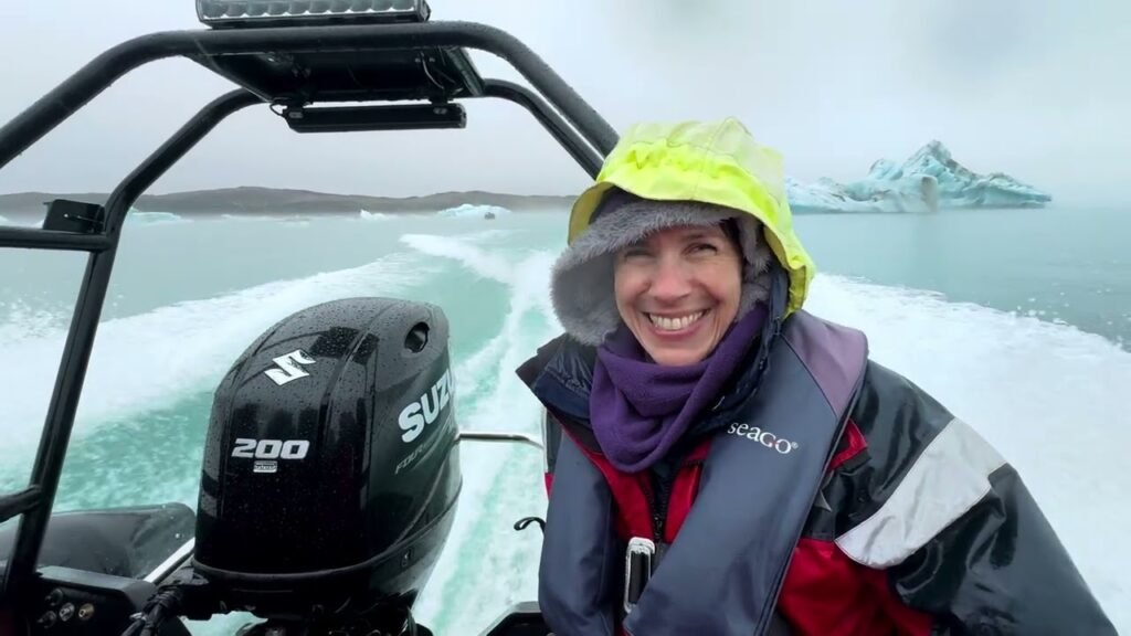 A smiling traveler wearing a bright yellow hood is pictured on a boat with a 200 HP outboard motor in an icy sea, with snow-covered islands in the background.