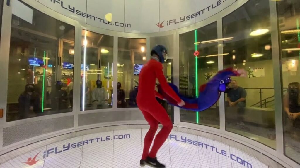An instructor in a red suit guides a guest in a blue suit during indoor skydiving at iFLY Seattle.