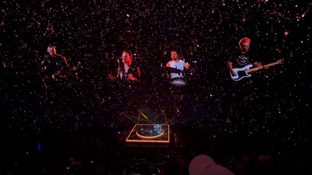 A live concert with multiple performers on stage under vibrant, star-like lighting.