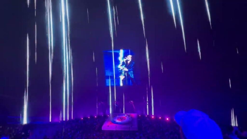 A live concert scene illuminated by intense purple and blue laser beams.