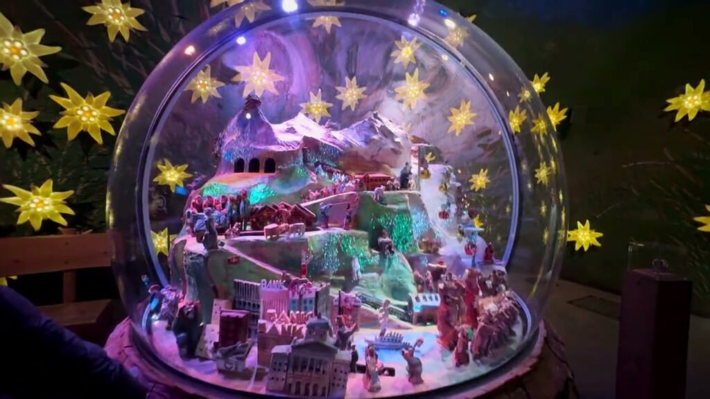 A large illuminated snow globe displaying a Christmas village scene with yellow star lights.
