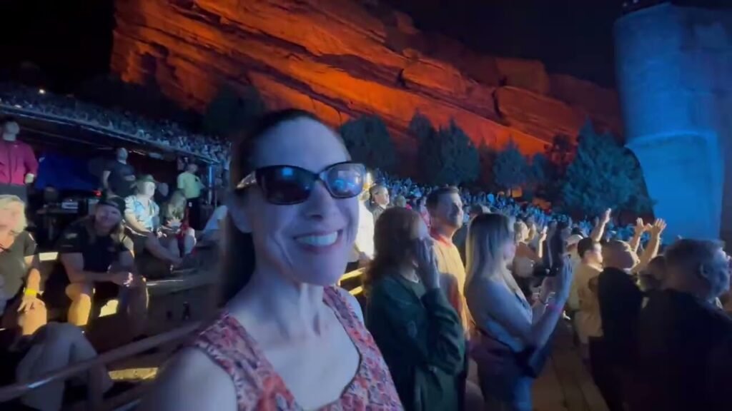 A woman smiling in front of a colorful nighttime light show projected on canyon walls.