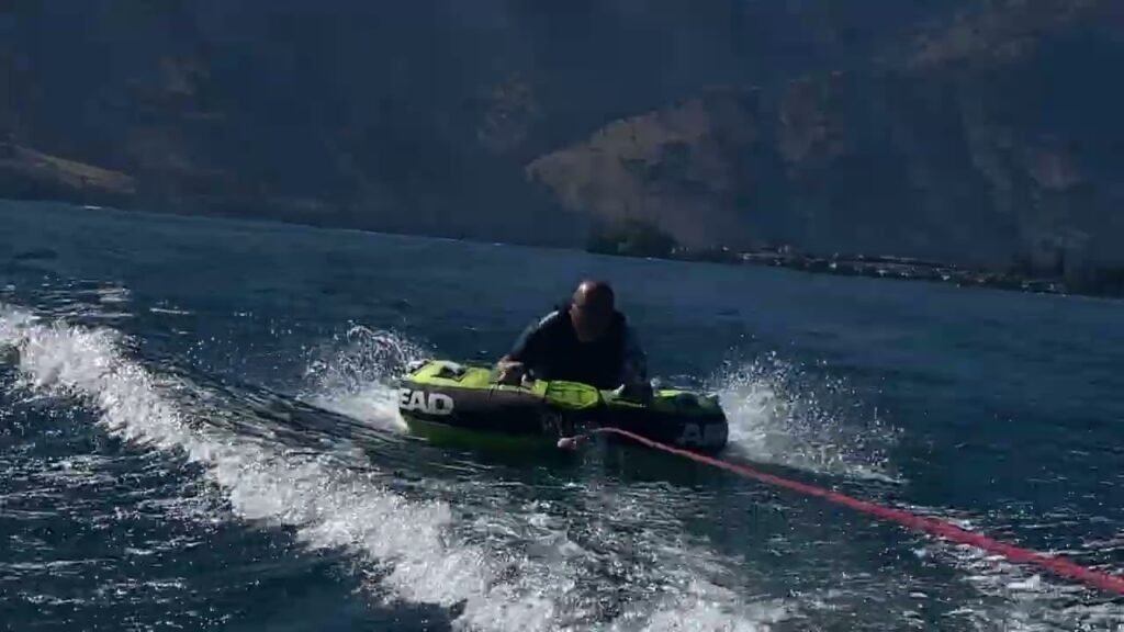 A person performs an aquaplaning trick on a green wakeboard behind a boat.