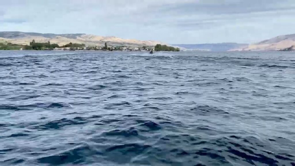 A wide shot of gentle ocean waves with a hilly, vegetated shoreline in the background.