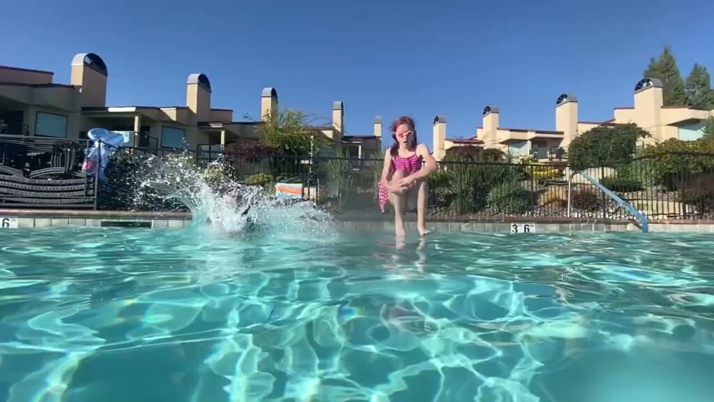Person enjoying a sunny day in a hotel pool with clear blue water andplashes in the background.