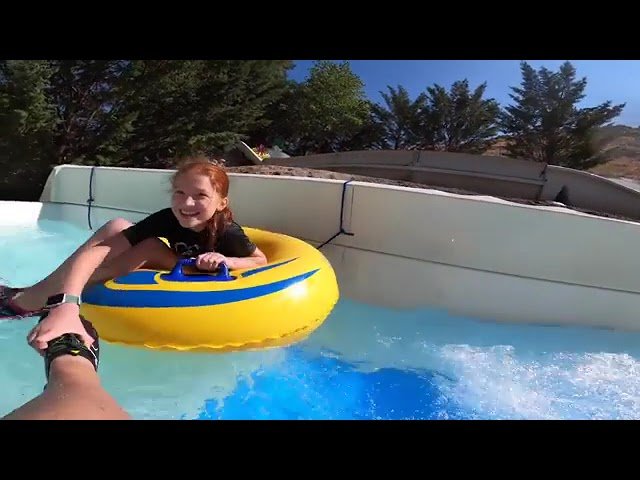 A person relaxing in a yellow inner tube on a lazy river with palm trees in the background.